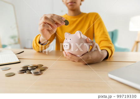 Saving money investment for future. African american girl holding pink piggy bank and putting money coin. Saving investment budget business wealth retirement financial money banking concept Saving money investment for future. African american girl holding pink piggy bank and putting money coin. Saving investment budget business wealth retirement financial money banking concept 99719330