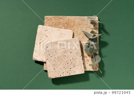 Travertine tile. Minimal composition, empty mockup template for product presentation made with natural travertine and eucalyptus on a dark green background. Flat lay with copy space. Top view. Travertine tile. Minimal composition, empty mockup template for product presentation made with natural travertine and eucalyptus on a dark green background. Flat lay with copy space. Top view. 99721045