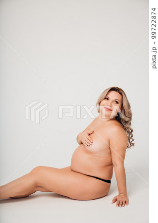 a naked pregnant against the background of a white cyclorama in a photo studio. a naked pregnant against the background of a white cyclorama in a photo studio. 99722874