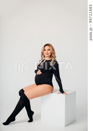 a beautiful and calm pregnant blonde in a black bodysuit in a white room. 99722883