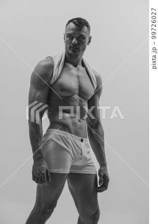 Black and white portrait of muscular male fashion model over grey studio background. Man posing shirtless. Masculinity. Concept of men's health, beauty, body and skin care, fitness. 99726027