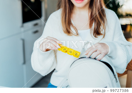 Woman putting daily pills organizer into her bag. Taking daily medicine antioxidant diet vitamin supplements for beauty skin hair health care medicament biohacking concept. Selective focus Woman putting daily pills organizer into her bag. Taking daily medicine antioxidant diet vitamin supplements for beauty skin hair health care medicament biohacking concept. Selective focus 99727386