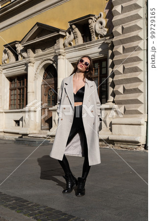 Street style, autumn, spring fashion concept: fashionable woman wearing luxury beige coat, sunglasses, wide leg black leggings, ankle bots, walking in street 99729165
