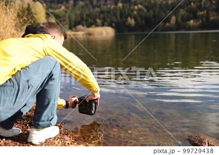 Man taking photo of lake using professional camera Man taking photo of lake using professional camera 99729438
