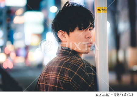 夜の街でポールに寄りかかる男性 99733713