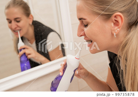 A woman with braces on her teeth uses an irrigator. Close-up portrait.  99735878