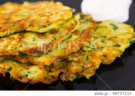 Zucchini pancakes with sour cream on black plate 99737215