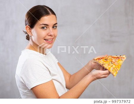 Pleased young woman holding piece of pizza 99737972