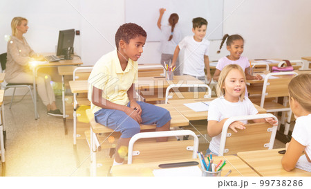 Positive primary school students are talking about homework at desk 99738286
