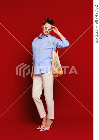 Woman with oranges in reusable string bag over the shoulder touching her sunglasses 99743762