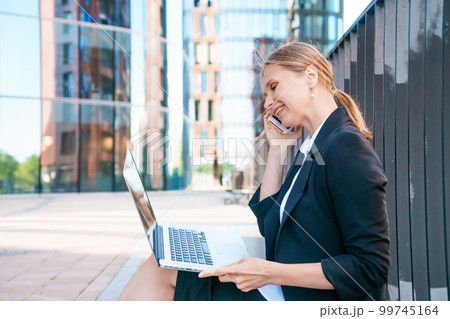 Business woman working on street. Young woman is sitting on bench with laptop 99745164