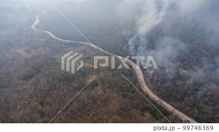 Aerial drone view of a wildfire burning through a forest area, fills the sky with dark smoke in the woods near the edge of the highway. Burning Forest. Air pollution concept Aerial drone view of a wildfire burning through a forest area, fills the sky with dark smoke in the woods near the edge of the highway. Burning Forest. Air pollution concept 99746369