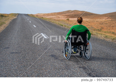 Woman in a wheelchair on a highway in the steppes. Woman in a wheelchair on a highway in the steppes. 99749733