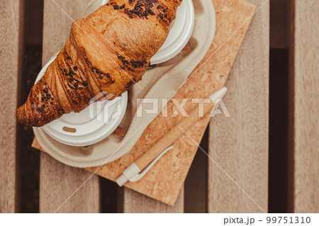 Fresh baked chocolate croissant on Two paper cups with lid for tea to go. Empty paper notebook. Freelancer's place of work. Study and work online. Remote business education. Making plans for next week 99751310