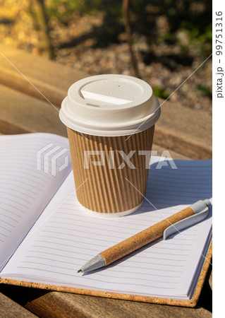 Eco recycling paper cup with coffee or tea on kraft paper with empty paper notebook on wooden bench. Concept of study work outdoors. Take away coffee to go. Copy space for text. Disposable Cardboard Eco recycling paper cup with coffee or tea on kraft paper with empty paper notebook on wooden bench. Concept of study work outdoors. Take away coffee to go. Copy space for text. Disposable Cardboard 99751316
