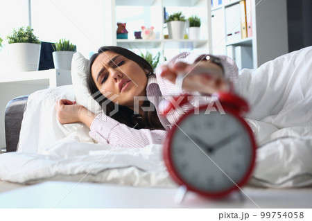 Dissatisfied woman lies in bed and turns off alarm clock. Dissatisfied woman lies in bed and turns off alarm clock. 99754058