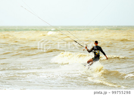 A young kiteboarder rides the waves into the sea A young kiteboarder rides the waves into the sea 99755298