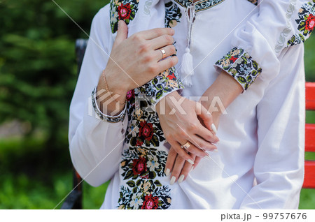 Golden wedding rings on the hands of the newlyweds. Man and woman in national Ukrainian clothes. Bridal bouquet with white flowers 99757676