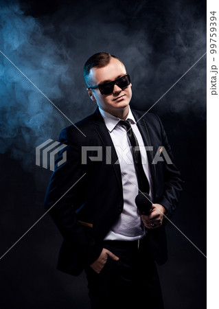 Stylish man holding microphone on dark background with smoke, actor, singer, show, host of the event Stylish man holding microphone on dark background with smoke, actor, singer, show, host of the event 99759394