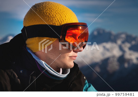 Male skier overlooking snow covered mountains on a sunny day, sun beams reflection in ski goggles 99759481