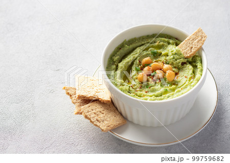 avocado hummus in white bowl with chickpeas, parsley, spices and rice crackers 99759682
