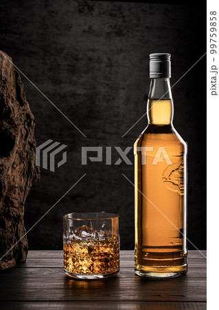 Bottle of whisky and glass with ice on wooden table with dark background with copy space. Vertical format. Bottle of whisky and glass with ice on wooden table with dark background with copy space. Vertical format. 99759858