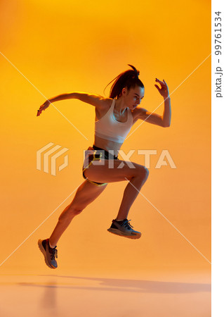 Dynamic portrait of young sportive girl, athlete, runner in motion, training over orange studio background in neon light. Concept of sport. health and strength Dynamic portrait of young sportive girl, athlete, runner in motion, training over orange studio background in neon light. Concept of sport. health and strength 99761534