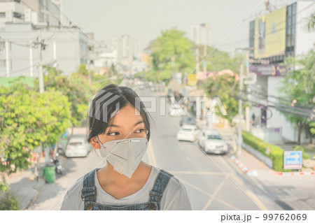 Health care concept. Young girl in face mask on city street, Asian girl wearing the N95 Respiratory Protection Mask against PM2.5 air pollution and headache Suffocate. Health care concept. Young girl in face mask on city street, Asian girl wearing the N95 Respiratory Protection Mask against PM2.5 air pollution and headache Suffocate. 99762069