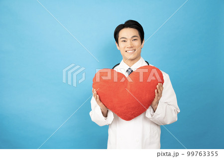 ブルーバックで赤いハートを持って微笑む男性医師の写真素材 [99763355  