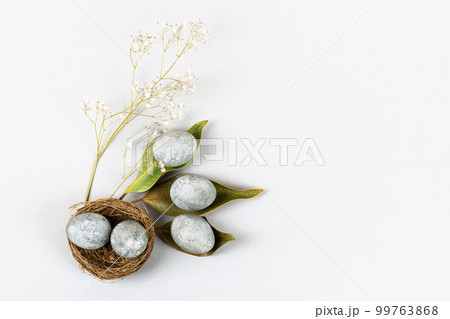 Minimal ecological Easter concept with dried flowers. Gray eggs on dry magnolia leaves and in a brown nest of twigs on a gray background Minimal ecological Easter concept with dried flowers. Gray eggs on dry magnolia leaves and in a brown nest of twigs on a gray background 99763868