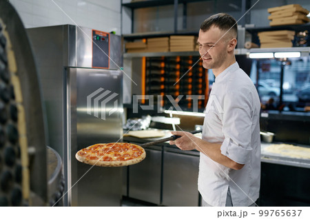 Cheerful young man working in pizza shop presenting fresh baked pastry Cheerful young man working in pizza shop presenting fresh baked pastry 99765637