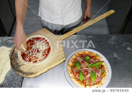 Above view on chef hand preparing pizza base on professional kitchen Above view on chef hand preparing pizza base on professional kitchen 99765640