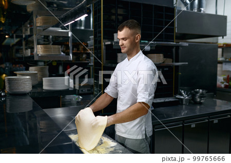 Chef tossing dough in air while making pizza base Chef tossing dough in air while making pizza base 99765666