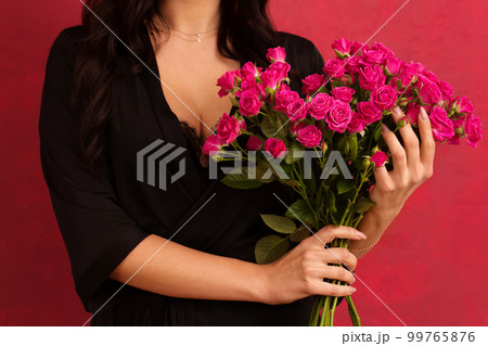 A woman in a black dressing gown with a deep neckline holds a bouquet of pink roses, on a pink background, close-up 99765876