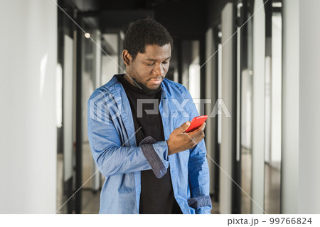 African American serious man using red mobile phone in office building, internet, broadband, 5G. Portrait of pensive african american man in office 99766824