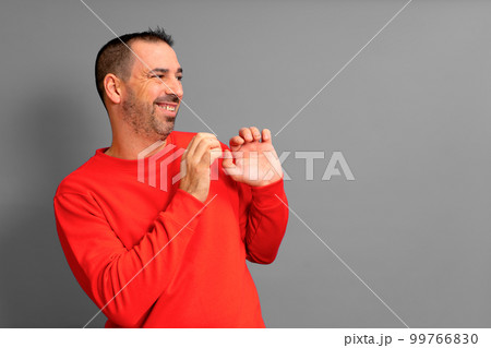 Hispanic man in his 40s wearing a red sweater poses embarrassed to the side with his hands in a defensive position, isolated on gray background. Hispanic man in his 40s wearing a red sweater poses embarrassed to the side with his hands in a defensive position, isolated on gray background. 99766830