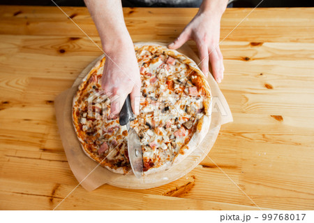 Closeup hand of chef baker in uniform blue apron cutting pizza at kitchen 99768017