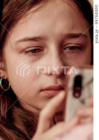 A teenage girl is crying looking at a smartphone. A teenage girl is upset. 99768900