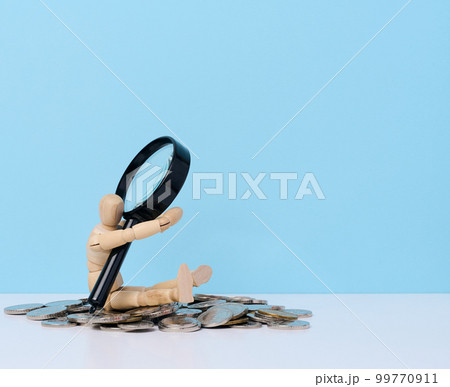 A wooden mannequin is holding a stack of coins against the background of a magnifying glass. The concept of income growth 99770911