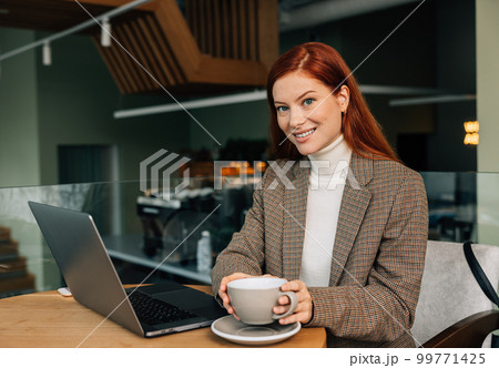Beautiful businesswoman with ginger hair looking at camera while holding a cup 99771425