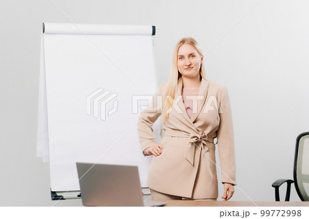 a blonde in a suit in an office with a board for meetings, desktop and laptop 99772998