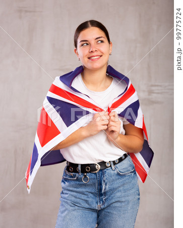 Joyous young woman holding Britain flag against unicoloured background 99775724