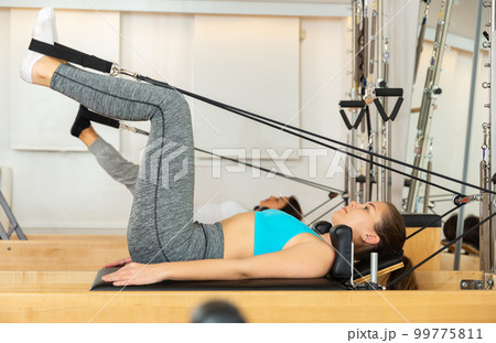 Young woman performing pilates on reformer in fitness studio 99775811