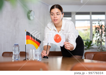Young female attendant putting up flags for international negotiations between germany and japan 99776034