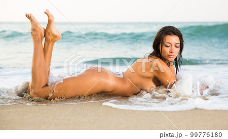 Portrait of sexy nude girl playfully lying on the sandy beach 99776180