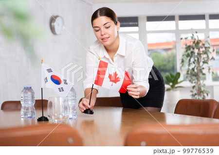 Young female attendant putting up flags for international negotiations between south korea and canada 99776539
