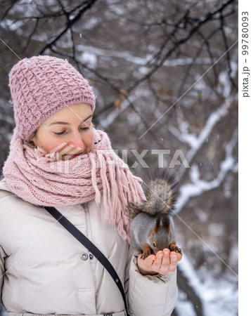 Girl feeds a squirrel with nuts at winter. Caring for animals in winter or autumn. 99780093