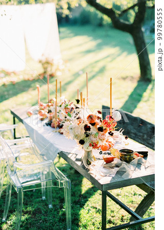 Laid table with candles and treats near chairs and benches in the garden Laid table with candles and treats near chairs and benches in the garden 99780555