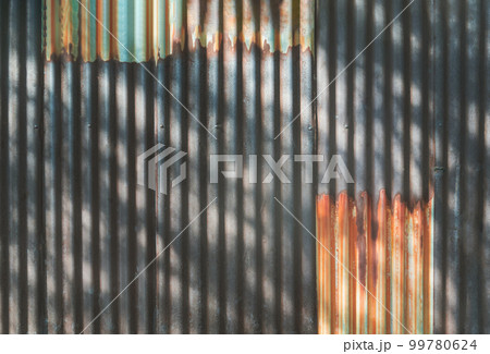 Artistic of old and rusty zinc sheet wall with The shadow of the bright sunlight shining through trees and leaves beautifully. 99780624