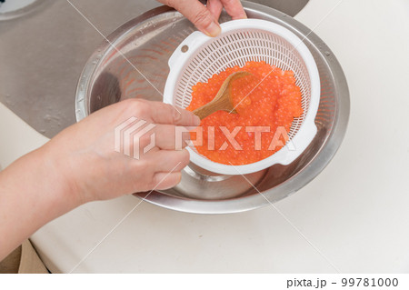 【イクラの醤油漬けを作るために、洗い終わった生イクラをスプーンでお酒を馴染ませる】 【イクラの醤油漬けを作るために、洗い終わった生イクラをスプーンでお酒を馴染ませる】 99781000